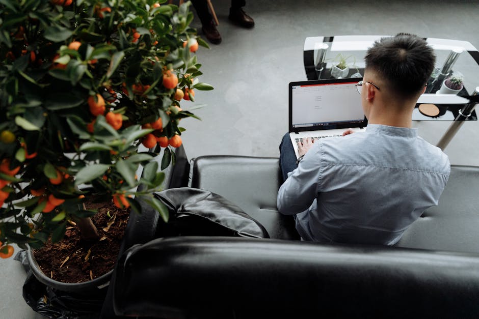 Man with glasses stretching his back while sitting at an office desk with a computer.