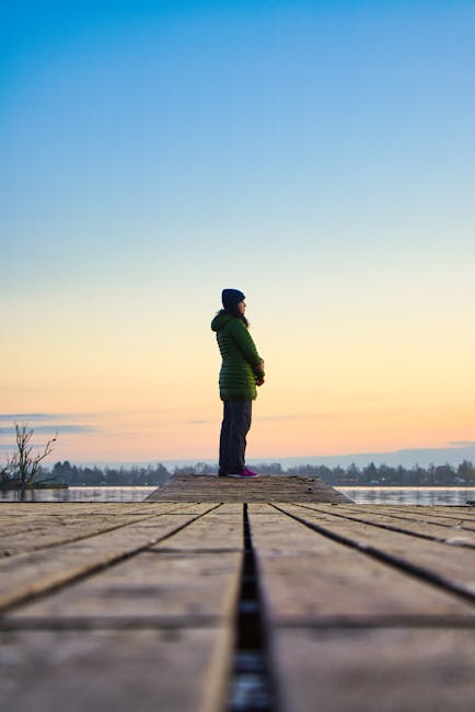 Woman in a peaceful yoga pose on a wooden dock by a calm lake at sunrise.